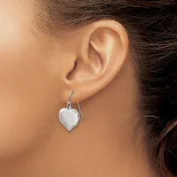 A person wearing a silver heart-shaped dangle earring on a fish hook wire, shown from the side profile of their ear and neck.