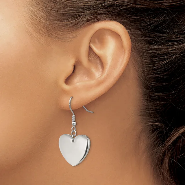 A person wearing a silver-toned heart-shaped dangle earring on a fish hook ear wire, shown from the side view of their ear and neck.