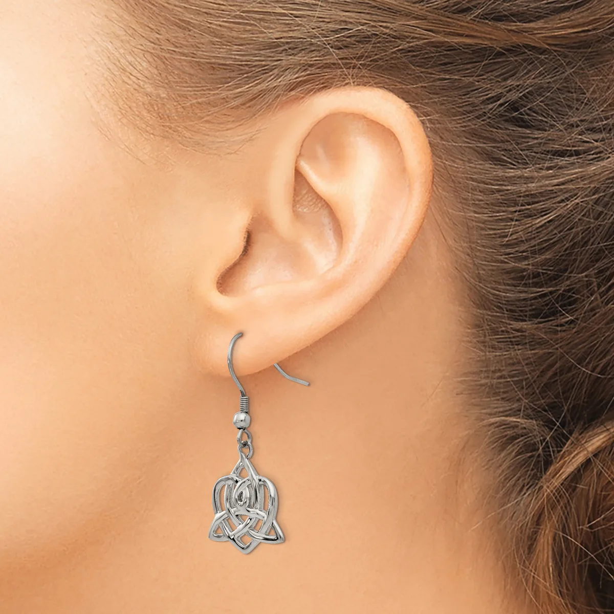 A woman wearing a silver-toned Celtic knot dangle earring with an ornate looped design, shown from the side view of her ear.
