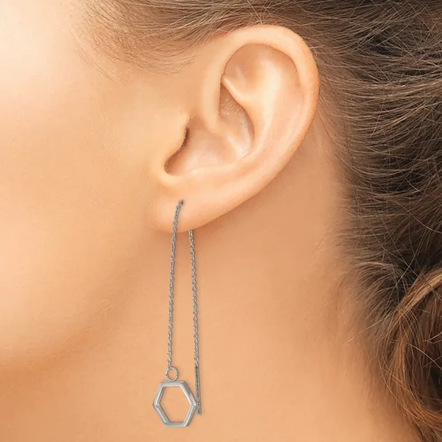 A person wearing a long silver chain threader earring with a small hexagonal pendant hanging from the end.
