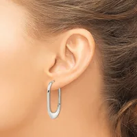 A person wearing a pair of polished silver oval hoop earrings, shown from the side view of their ear and neck.