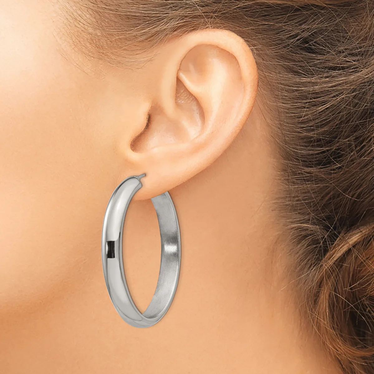 A woman wearing a pair of polished silver hoop earrings, shown from the side view of her ear and face.