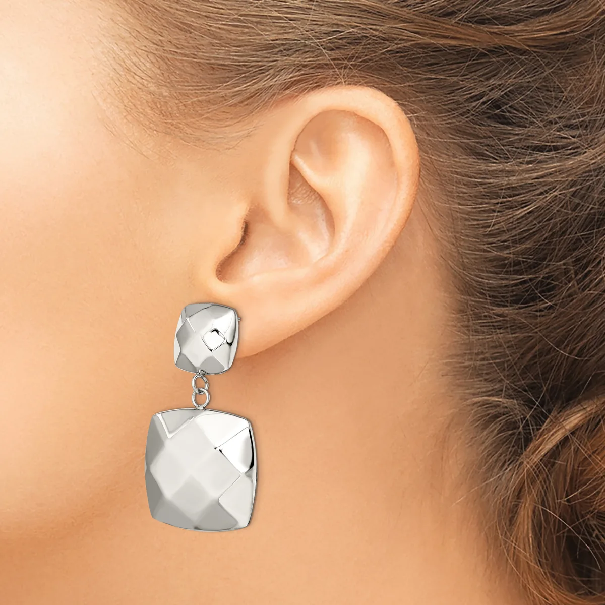 A woman wearing a silver two-tier dangle earring with geometric faceted square shapes hanging from her ear lobe.