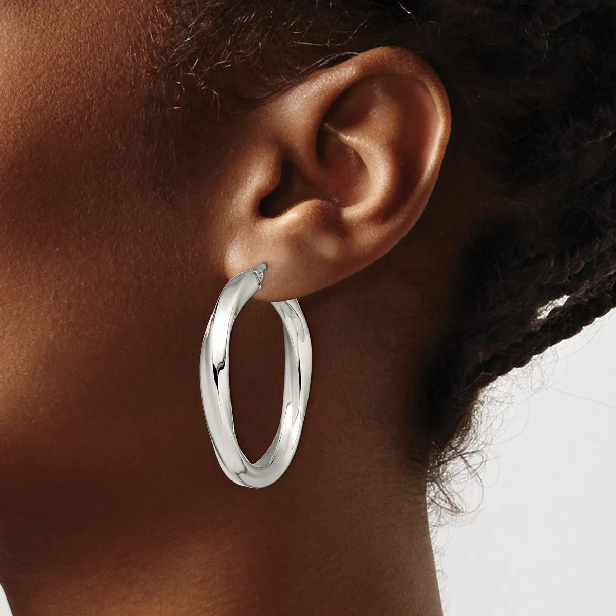 A person wearing large polished silver hoop earrings, shown in profile from the side of their face and neck.