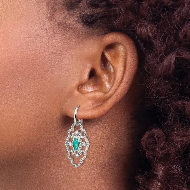 A silver drop earring with an emerald-cut turquoise stone surrounded by diamonds in a diamond-shaped setting, worn on a person's earlobe.