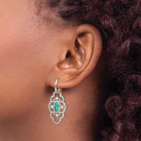 A silver drop earring with an emerald-cut turquoise stone surrounded by diamonds in a diamond-shaped setting, worn on a person's earlobe.