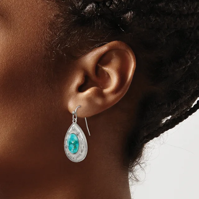 A woman wears a teardrop-shaped earring with a turquoise stone center surrounded by small white stones in a silver-toned metal setting.