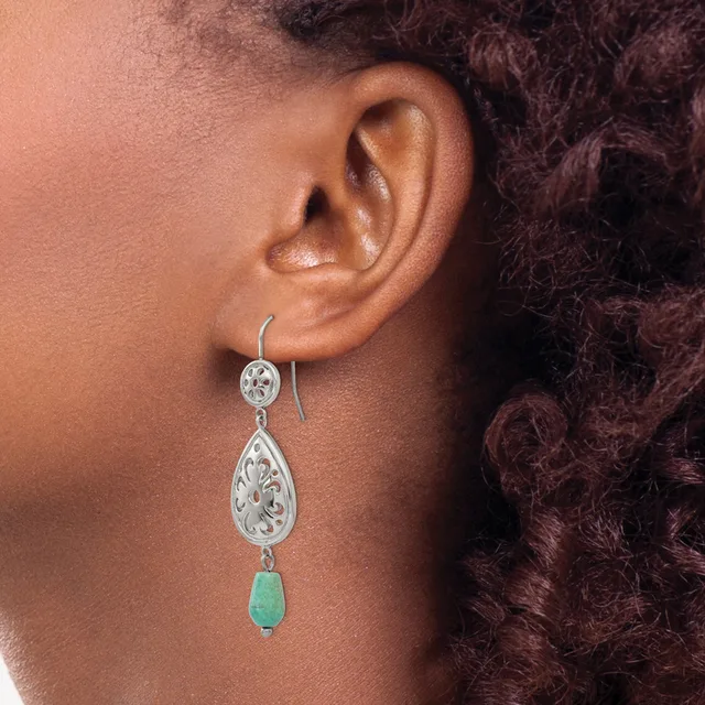 A woman wearing a dangling earring with a small circular silver top, ornate teardrop-shaped silver middle section, and green stone bottom piece.