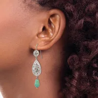 A woman wearing a dangling earring with a small circular silver top, ornate teardrop-shaped silver middle section, and green stone bottom piece.