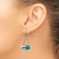 A pair of dangling earrings with silver-toned hooks holding two beads each—one polished silver sphere and one turquoise stone—displayed on a model's ear.