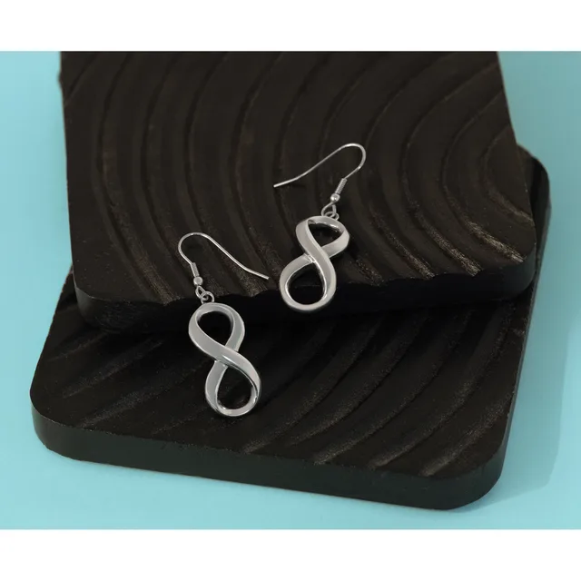 Pair of silver infinity symbol earrings with fish hook closures displayed on a black textured dish against a light blue background.