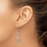 A silver infinity symbol dangle earring hangs from a woman's earlobe against her shoulder and brown hair.
