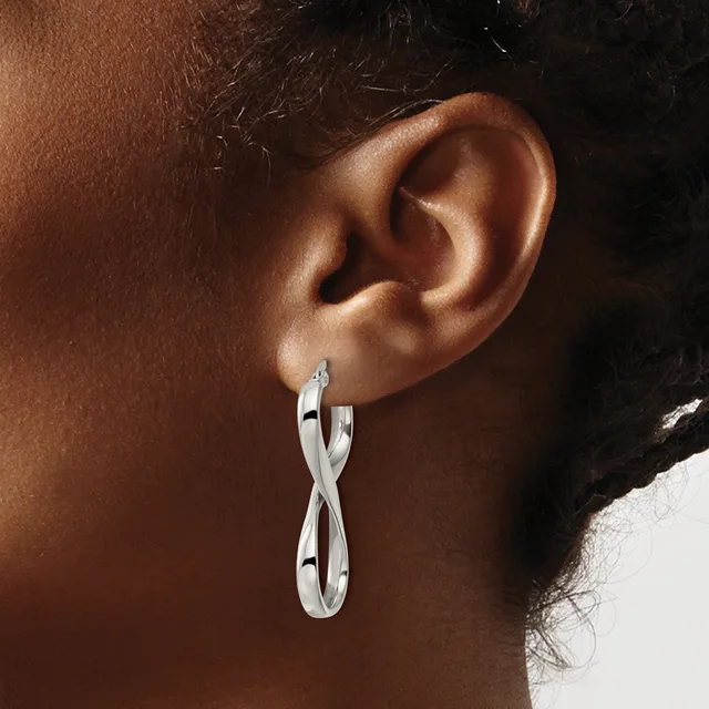 Close-up side view of a person's ear wearing a pair of twisted silver hoop earrings.