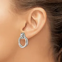 A silver knot-design earring with a hoop dangles from a pierced earlobe on a person with brown hair.