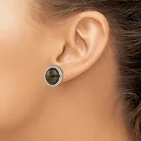 A close-up side view of a person's ear wearing a small oval stud earring with a dark green stone set in a silver-toned metal bezel.