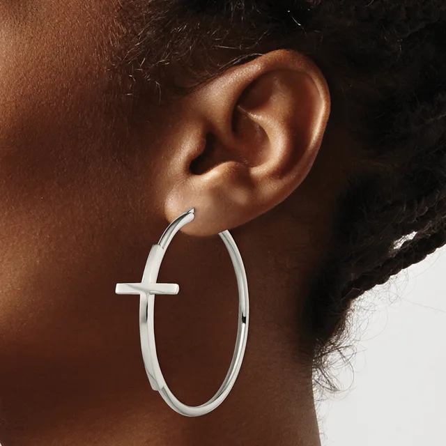 Close-up of a person's ear wearing silver hoop earrings with a cross cutout detail on the front.
