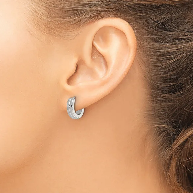 A woman wearing a small textured silver hoop earring in her earlobe, shown from the side view of her head and shoulder.
