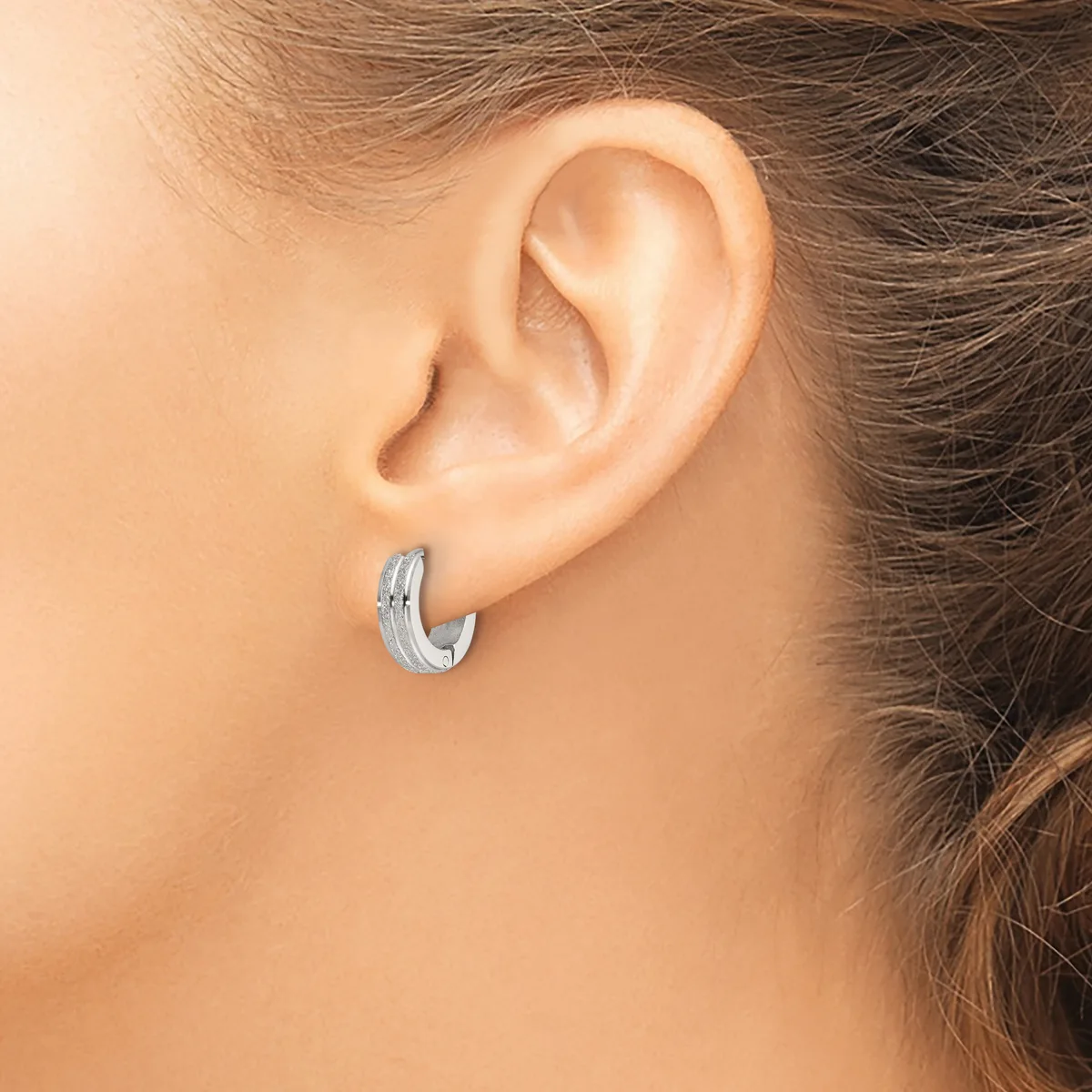 A woman wearing a small textured silver hoop earring in her earlobe, shown from the side view of her head and shoulder.