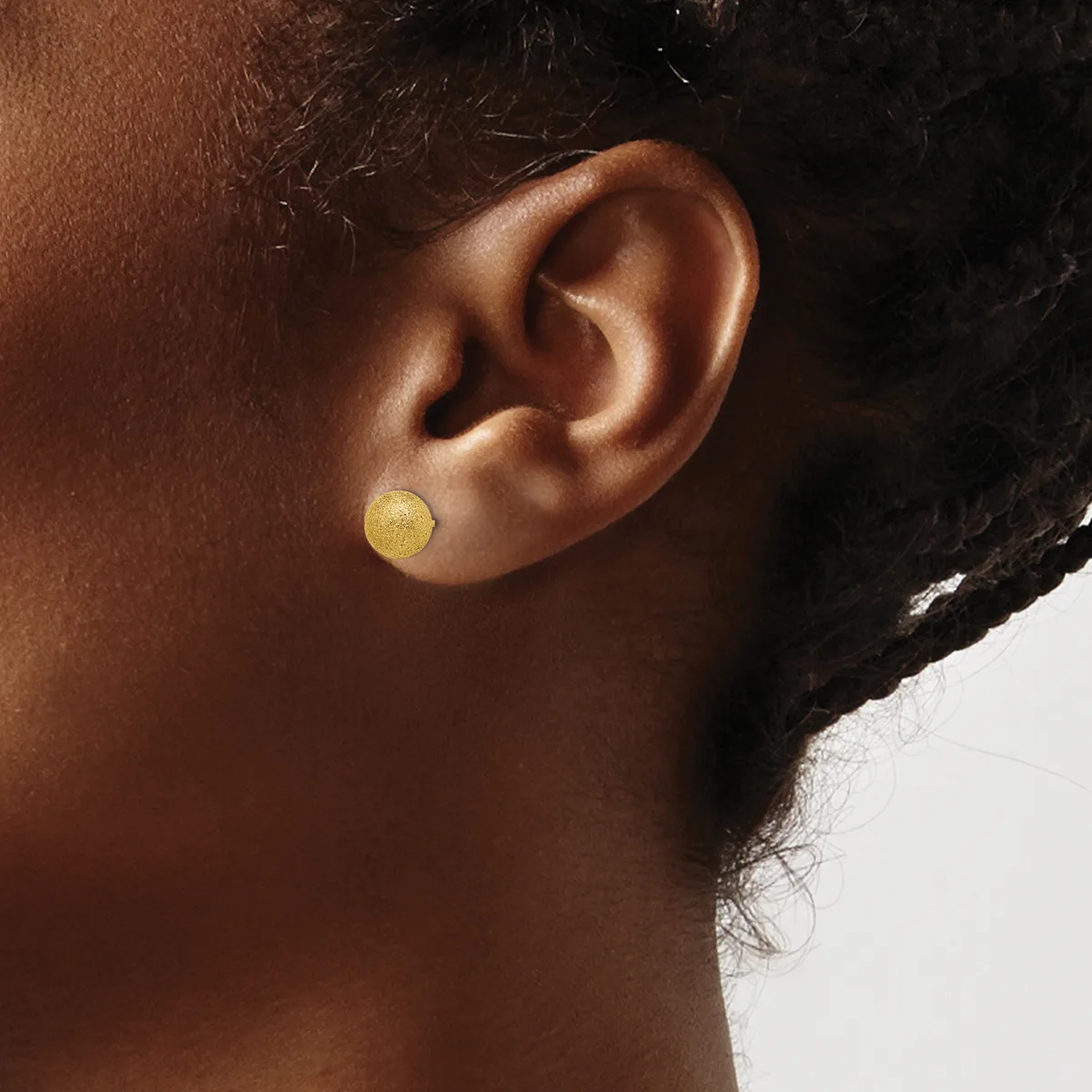 A person wearing a small round gold stud earring in their earlobe, shown in profile against a neutral background.