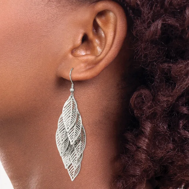 A silver leaf-shaped dangle earring with detailed vein texturing hangs from a curved wire hook on a person's earlobe.