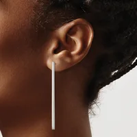 A person wearing a long, thin silver bar earring that hangs straight down from the earlobe.
