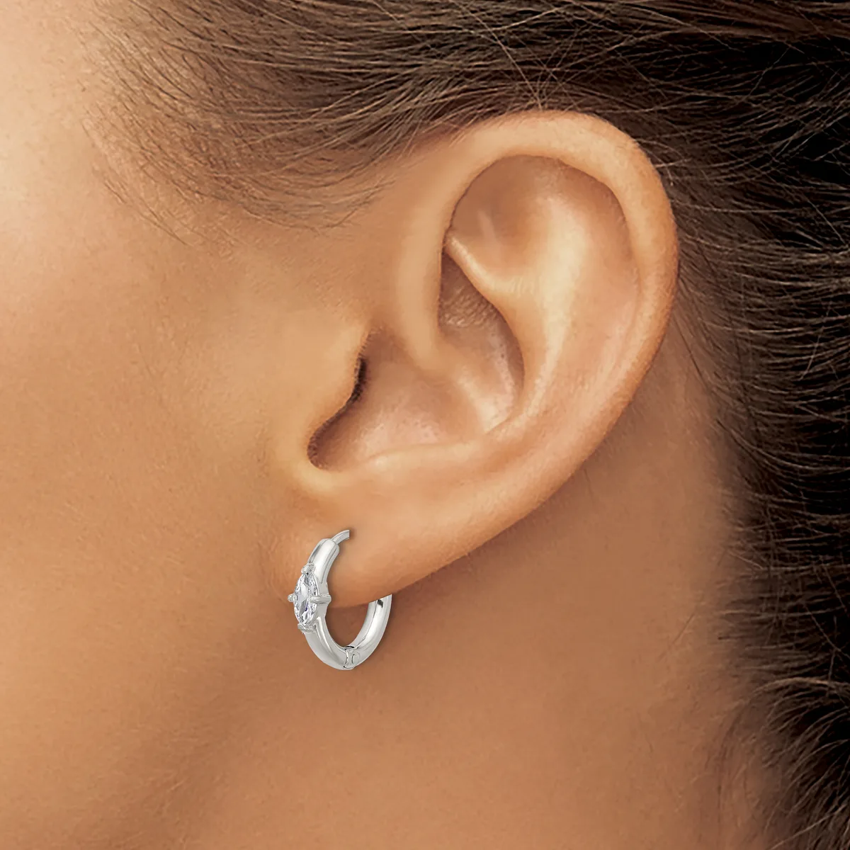 A person wearing a textured silver hoop earring in their earlobe, shown from the side profile of their face and ear.