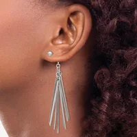 A person wearing a silver tassel dangle earring in their pierced ear lobe, with a small stud earring visible in the upper piercing.