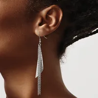 A person wearing long silver chain tassel earrings that hang from hook closures, shown from the side against a neutral background.