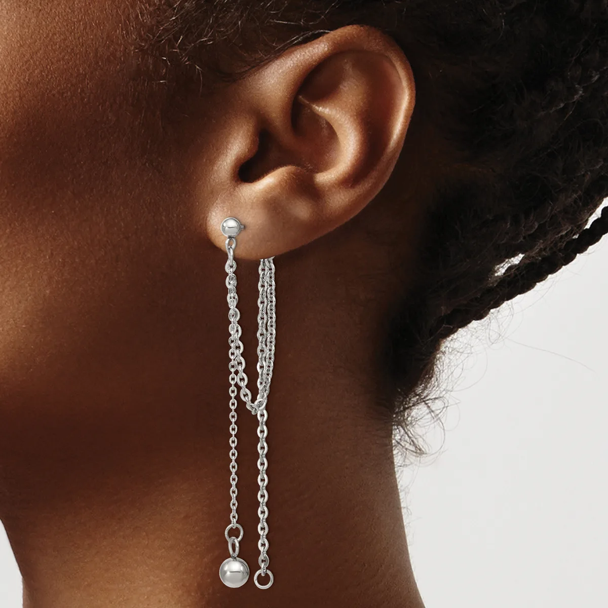 A person wearing a pair of long chain drop earrings with small pearl or ball terminals, shown from the side against a neutral background.