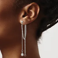 A person wearing a pair of long chain drop earrings with small pearl or ball terminals, shown from the side against a neutral background.