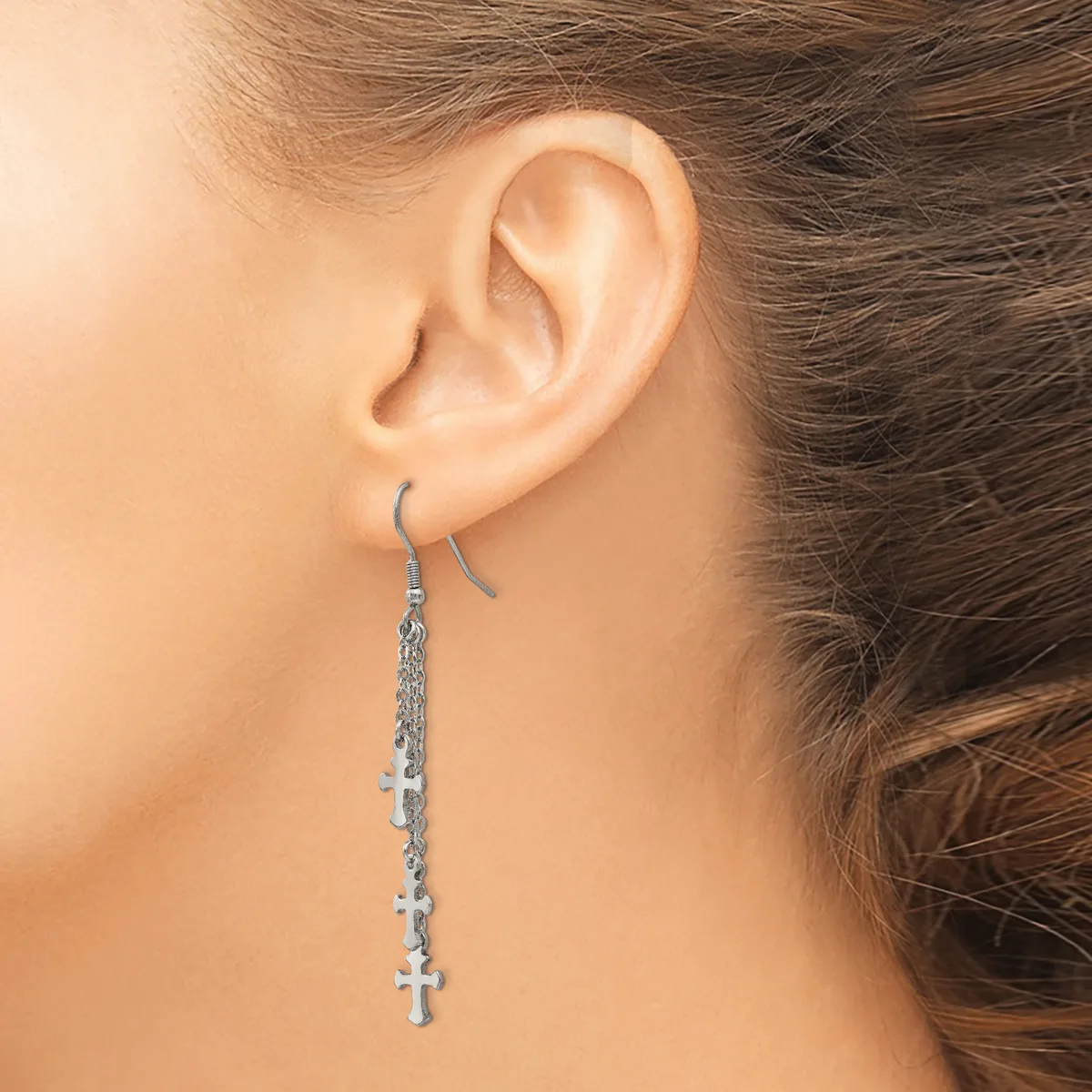 A person wearing a long dangling earring with small cross charms attached to a silver chain on a fish hook ear wire.