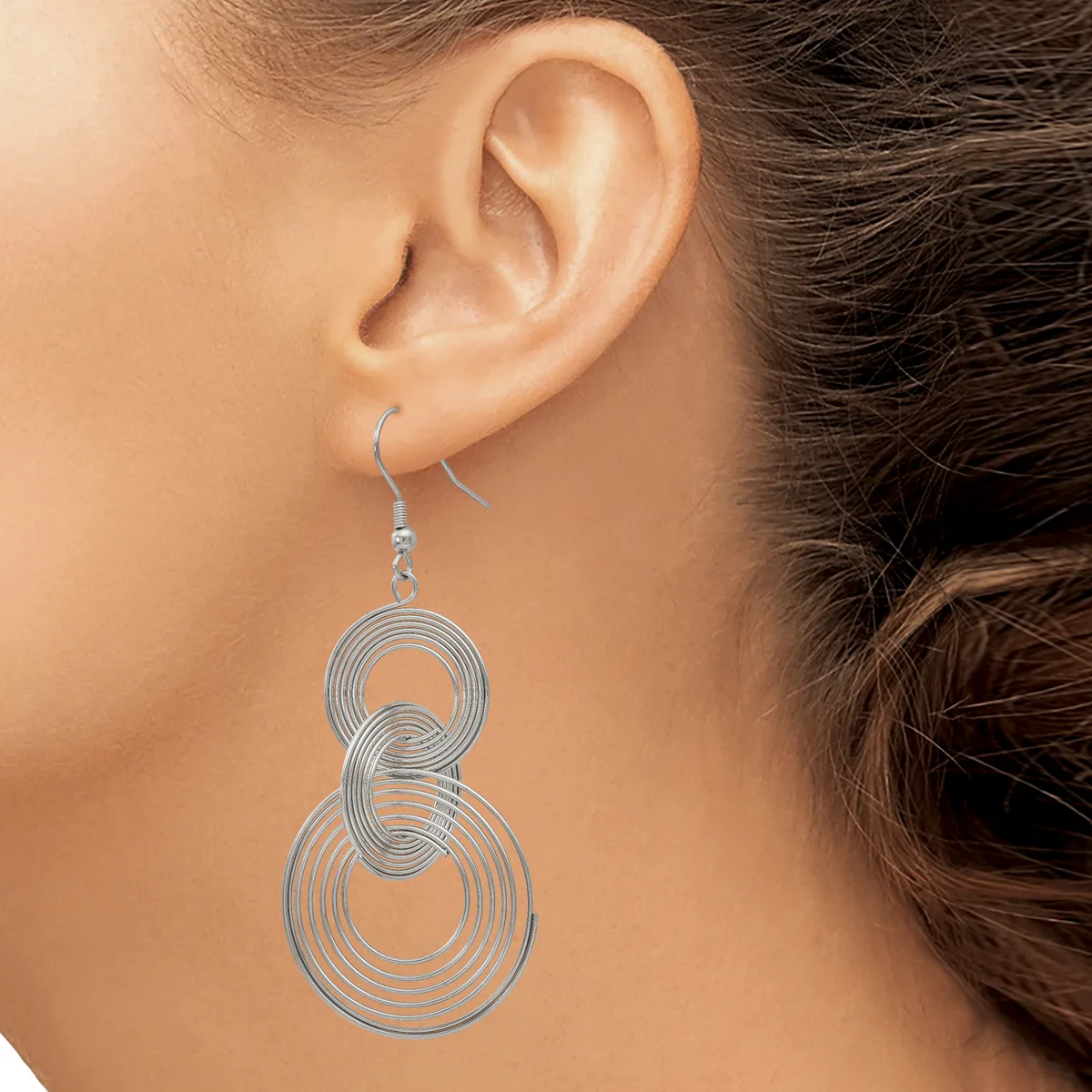 A woman wearing silver-toned spiral dangle earrings with concentric circular loops stacked vertically, shown from the side profile of her face and ear.