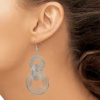 A woman wearing silver-toned spiral dangle earrings with concentric circular loops stacked vertically, shown from the side profile of her face and ear.