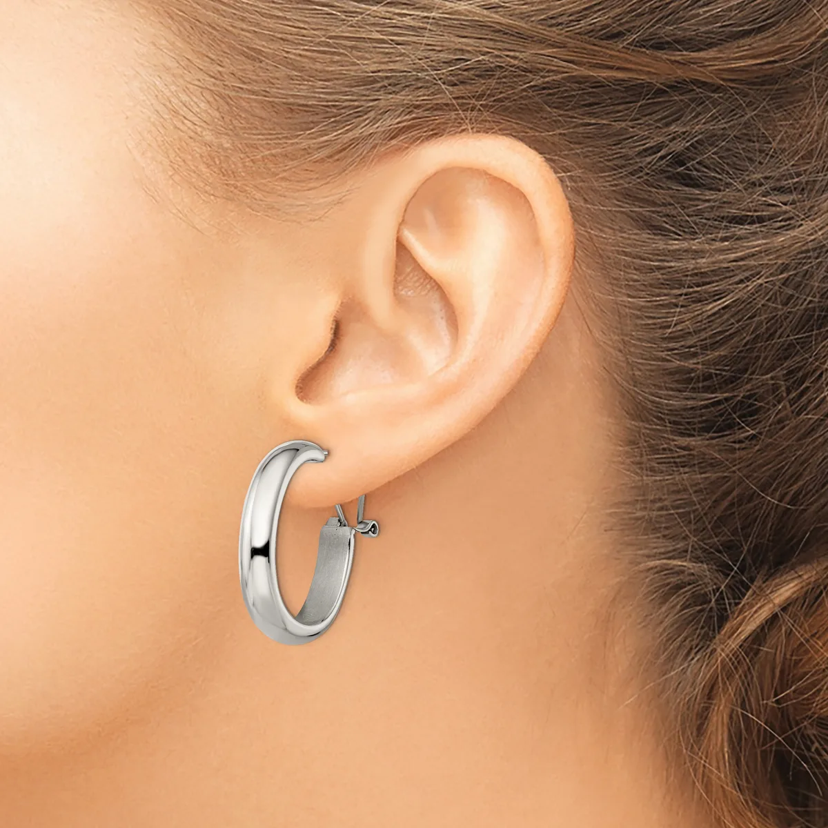A woman wearing a polished silver hoop earring with a small cross charm, shown from the side view of her ear and neck.