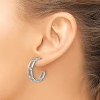 A silver textured hoop earring worn on a person's earlobe, shown from the side view.