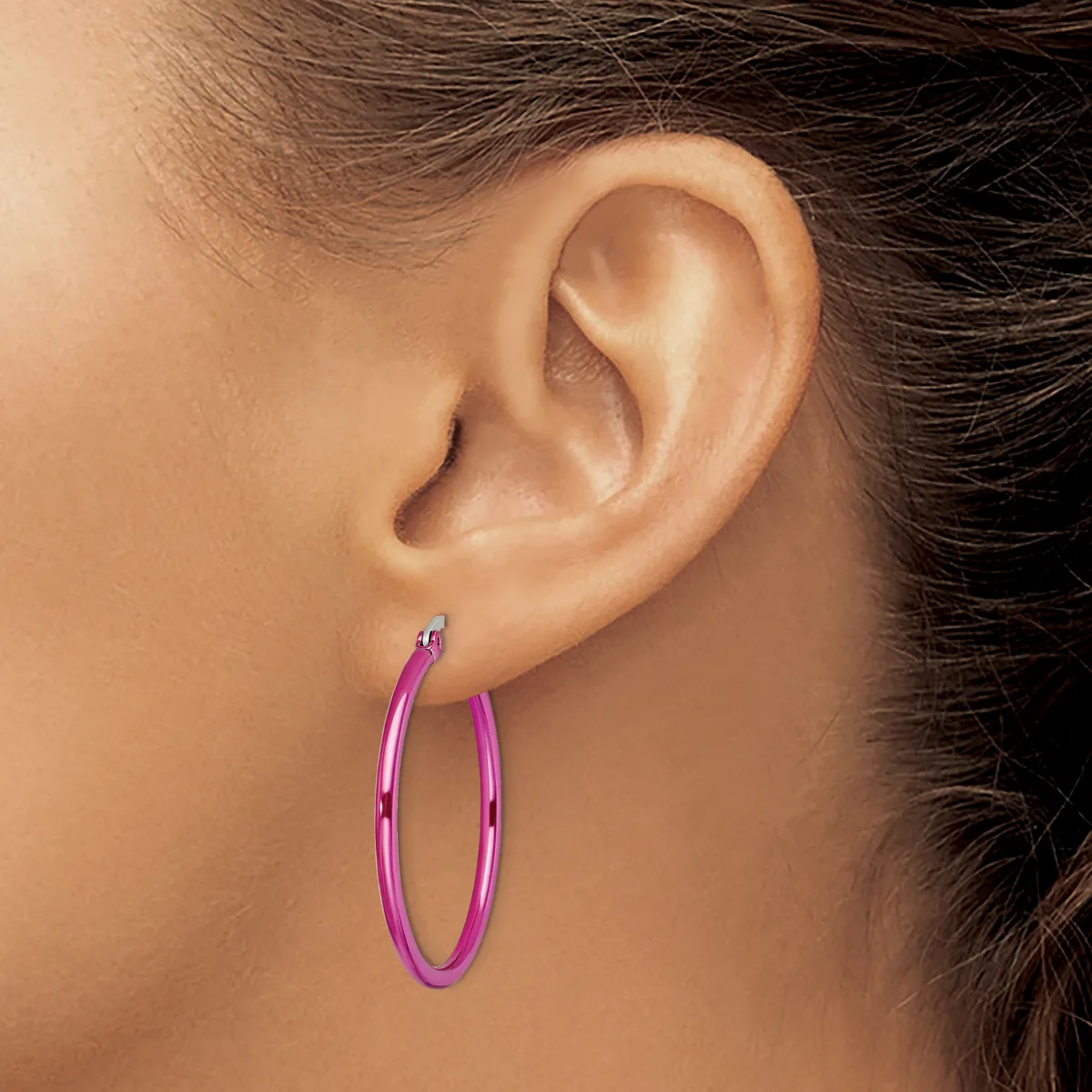 A person wearing a pair of pink metallic hoop earrings with a polished finish, shown in profile view against their ear.