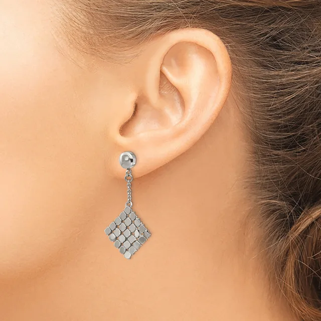 A woman wearing a silver-toned chain drop earring with a diamond-shaped pendant made of small square faceted stones hanging from her earlobe.
