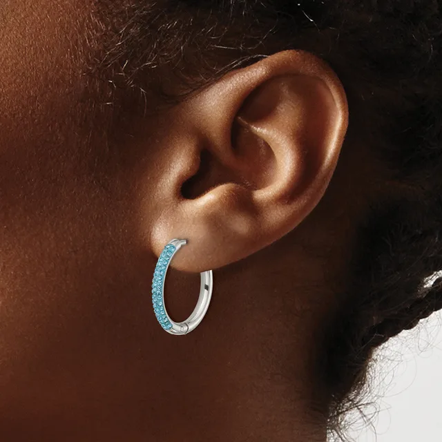 A person wearing a silver hoop earring with blue crystal or glitter coating on the front half, shown from the side profile against a dark background.