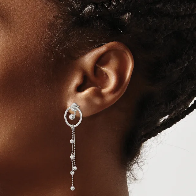 A woman wearing a silver drop earring with an oval hoop top and a chain of small beads hanging below, shown from the side against a neutral background.