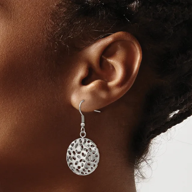 A woman wearing a silver filigree circular disc earring with an open lattice pattern hanging from a hook fastener on her earlobe.