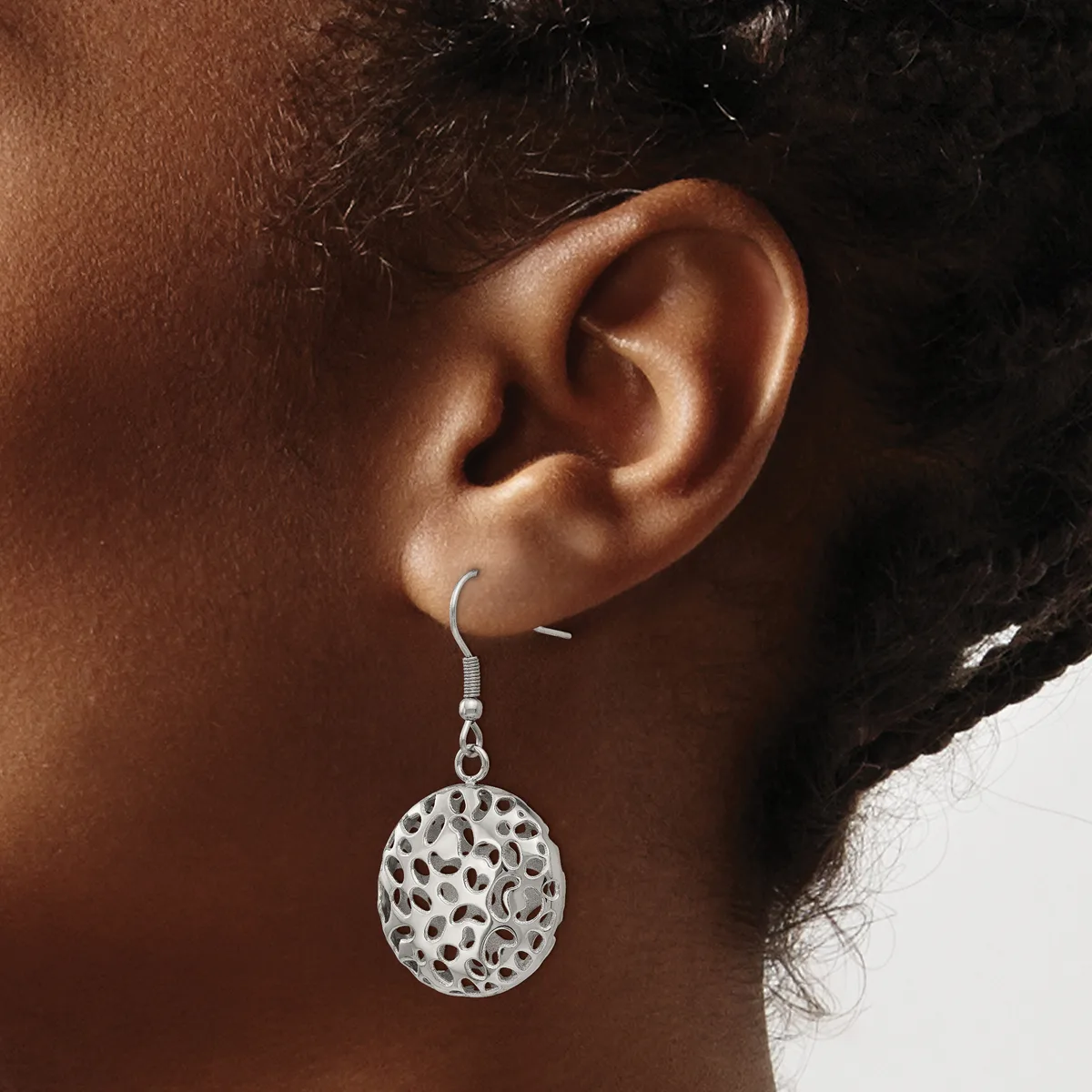 A woman wearing a silver filigree circular disc earring with an open lattice pattern hanging from a hook fastener on her earlobe.
