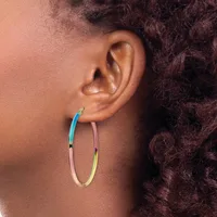 A person wearing a pair of large oval hoop earrings with a gradient color finish transitioning from blue to pink to yellow.