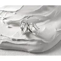 Two silver hoop earrings with rectangular clear crystal stones displayed on a textured white sculptural hand form against a light fabric background.