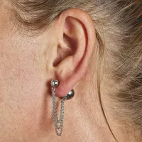 A woman's ear wearing two silver-toned earrings: a ball stud in the upper lobe and a curved bar with chain attachments in the lower lobe.