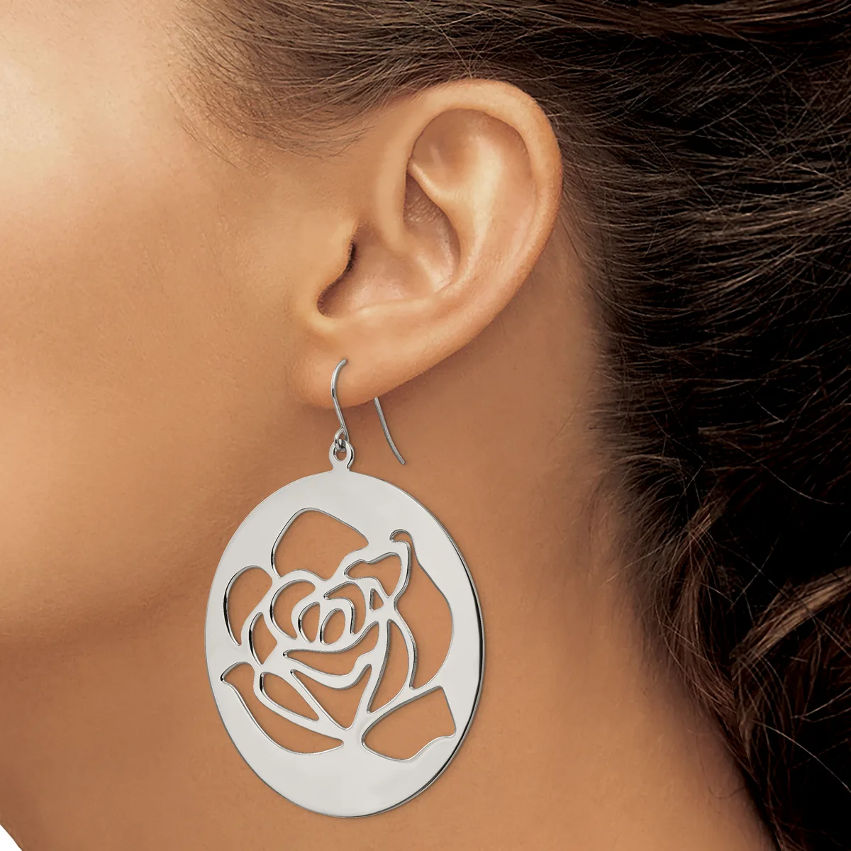 A woman wears a silver oval dangle earring with a cutout rose design, shown from the side view against her ear.