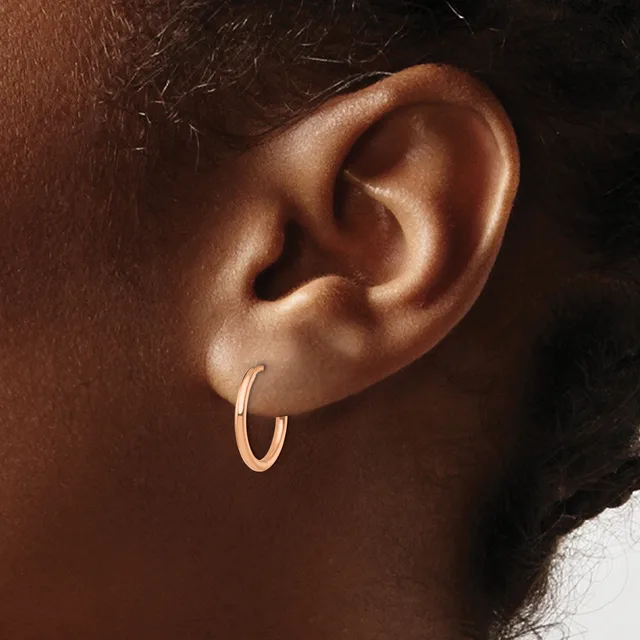 A small rose gold hoop earring worn in the earlobe of a person with deep brown skin tone.
