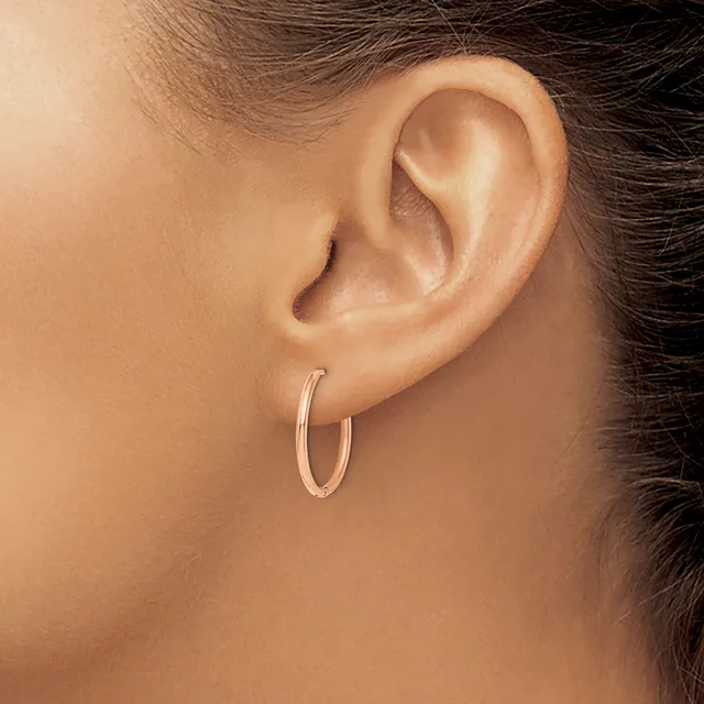 A person wearing a pair of polished silver hoop earrings, shown from the side profile with dark hair pulled back.