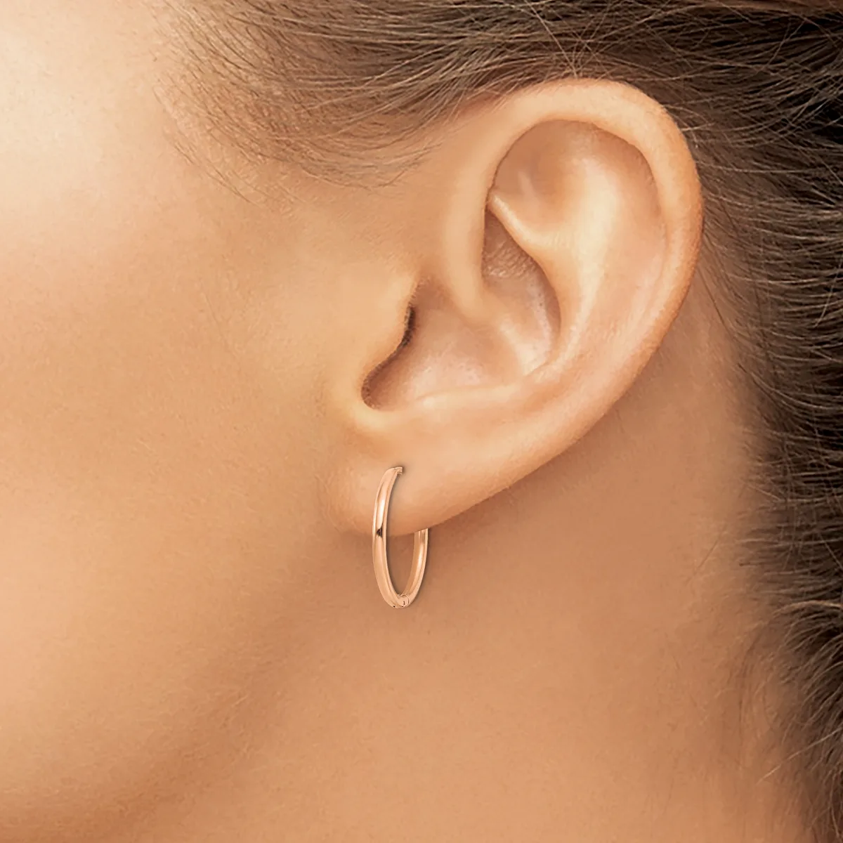 A person wearing a small polished silver hoop earring in their earlobe, shown in profile view.