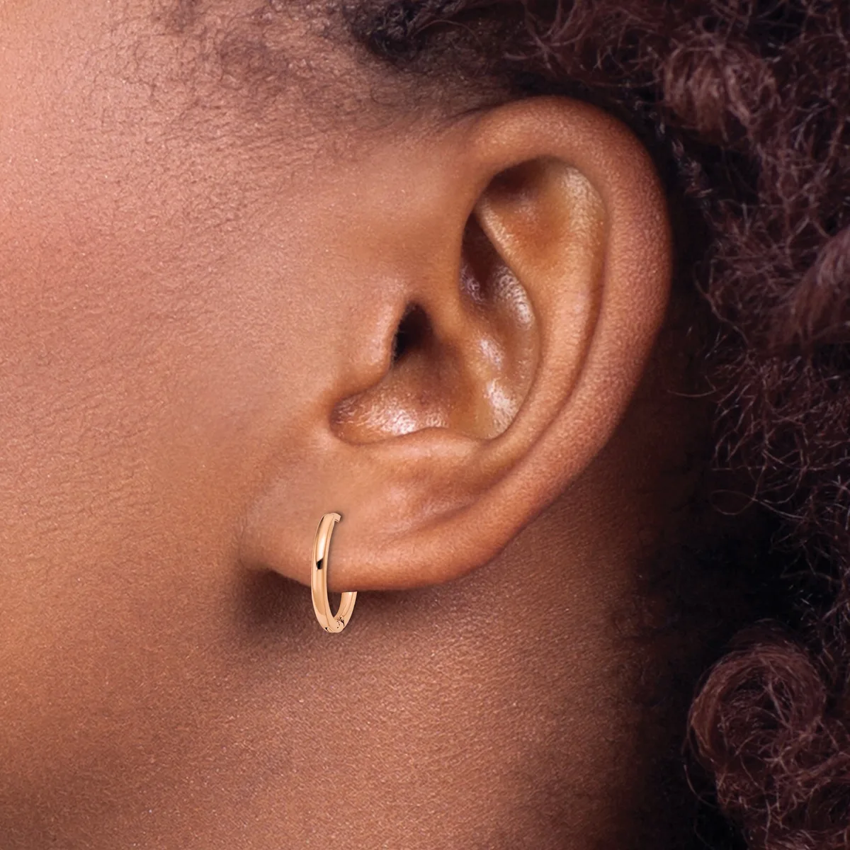 A person wearing a small gold hoop earring in their earlobe, shown in profile against their neck and shoulder.