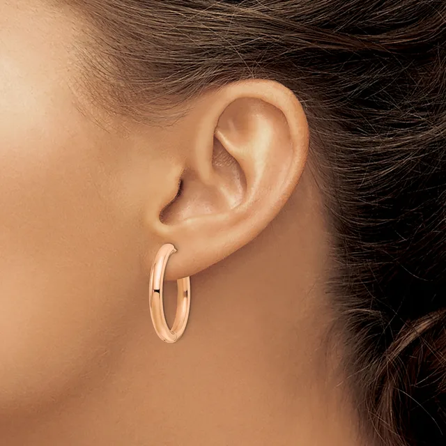 A person wearing rose gold hoop earrings with a polished finish, shown from the side profile with dark hair pulled back.